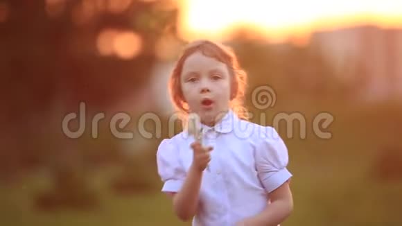 小女孩跑着玩他们吹蒲公英日落视频的预览图