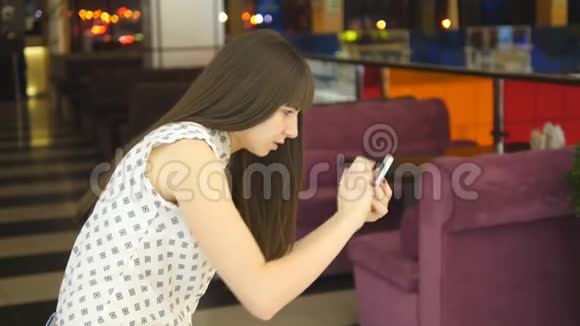 年轻女子在购物中心玩室内游戏使用智能手机女孩玩流行的智能手机游戏捕捉视频的预览图