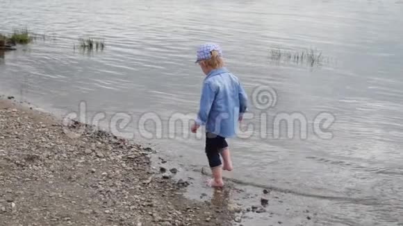 小男孩沿着河走那孩子在湖边跑慢动作快乐的婴儿在水边玩耍视频的预览图