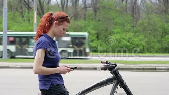 女孩坐在自行车上在智能手机上发短信视频的预览图