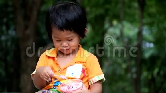 一个亚洲男孩正在公园里吃美味的纸杯蛋糕视频的预览图