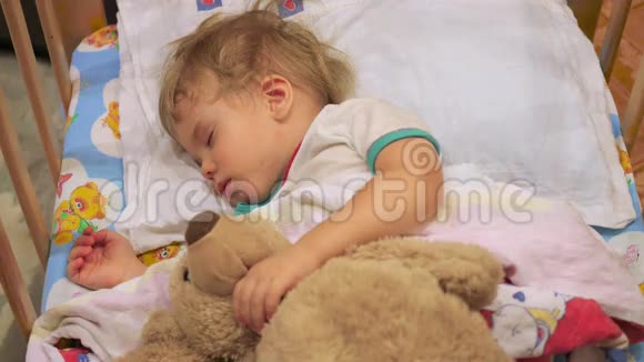 这个可爱的婴儿和一只泰迪熊睡在一张小床上视频的预览图