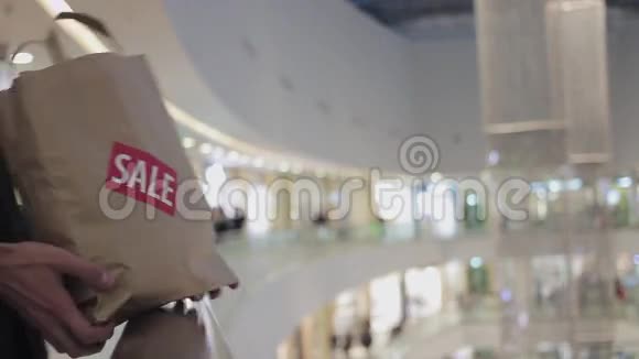 在商场的扶手上男士双手放着棕色的纸袋上面贴着红色的售货员视频的预览图