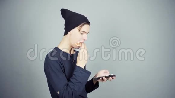 戴着黑色针织帽子的年轻人用智能手机吃披萨视频的预览图