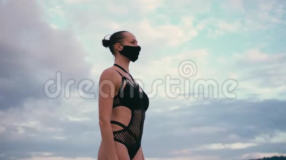 穿着黑色泳衣和医用防烟面具在海滨练习瑜伽的高加索女人视频的预览图