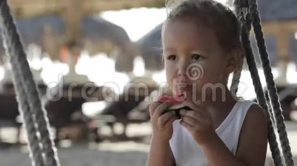 小可爱的小女孩坐在秋千上在沙滩上吃红色的西瓜视频的预览图