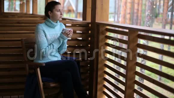 穿着蓝色毛衣的女孩坐在木椅上喝茶视频的预览图