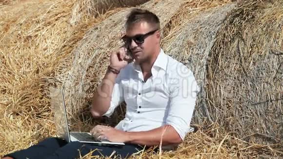 商人看起来很漂亮拿着笔记本电脑坐在干草堆里打电话暑假期间视频的预览图