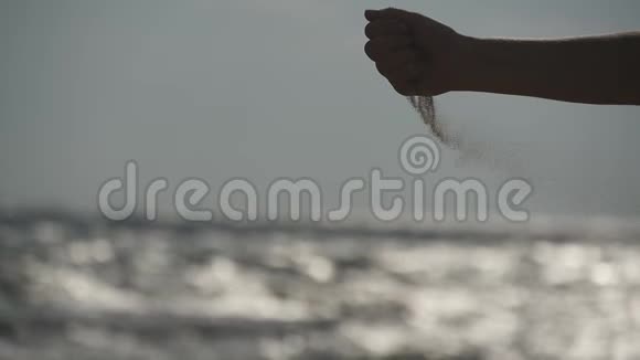 日落时分在海洋背景下女性用手在手指上撒着海沙带沙子的年轻女子手臂视频的预览图