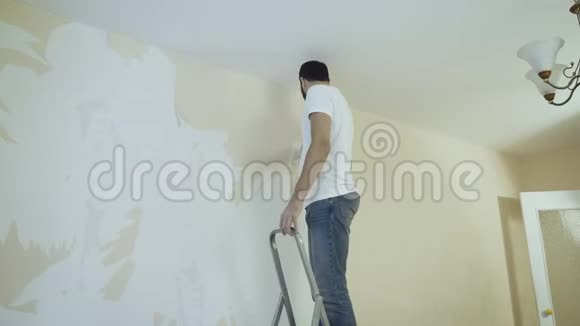 人在梯子上用刮刀在拆除壁纸的过程中视频的预览图