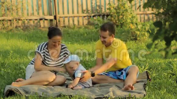 快乐的三口之家躺在夏日公园的草地上他们玩着微笑视频的预览图