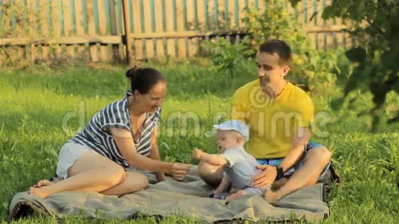 快乐的三口之家躺在夏日公园的草地上他们玩着微笑视频的预览图