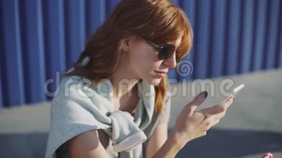 美丽的年轻女子在街上使用智能手机舔着彩色棒棒糖视频的预览图