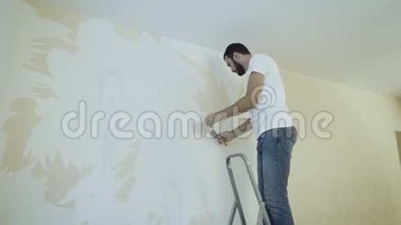人在梯子上用刮刀在拆除壁纸的过程中视频的预览图