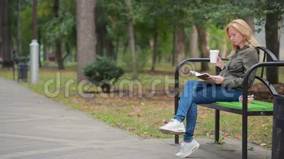 金碧辉煌的女子读书书在秋天的公园里喝热咖啡或茶视频的预览图