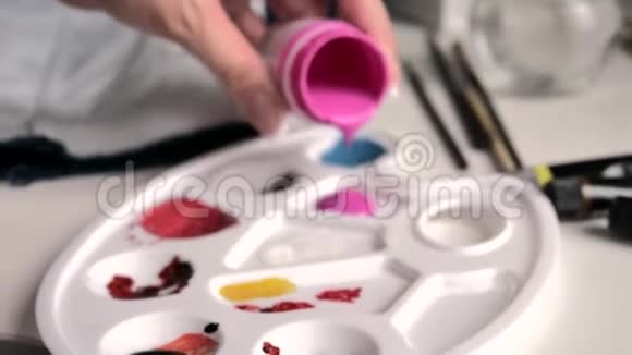 女人的手把粉红色的颜料倒入调色板拿起画笔在一杯水中冲洗在颜料中浸泡视频的预览图