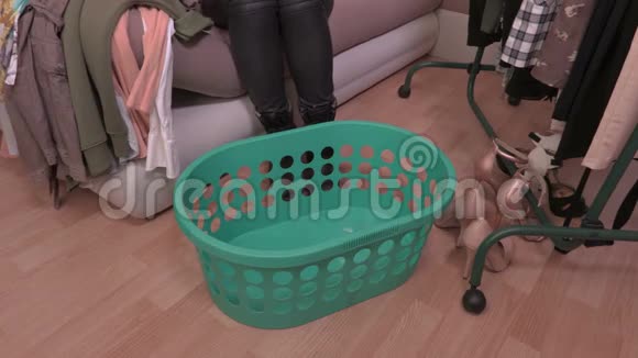 女人坐在靠近架子的沙发上把衣服放在塑料篮子里视频的预览图