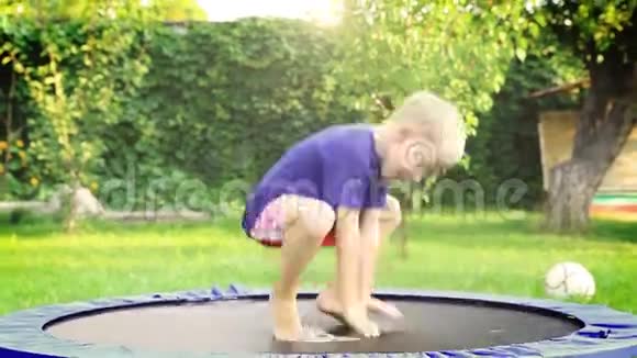 快乐的金发男孩在夏日花园的蹦床上跳视频的预览图