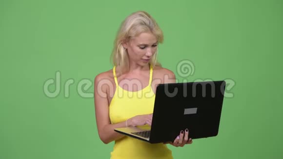 年轻快乐的金发美女在绿色背景下使用笔记本电脑视频的预览图