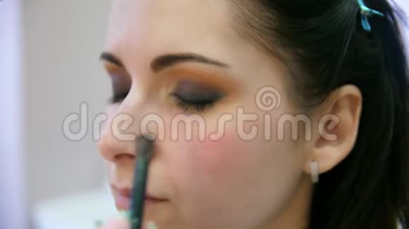 双手化妆师将化妆涂在一个年轻女人的脸上在专业沙龙里做眼妆的女孩晚上视频的预览图