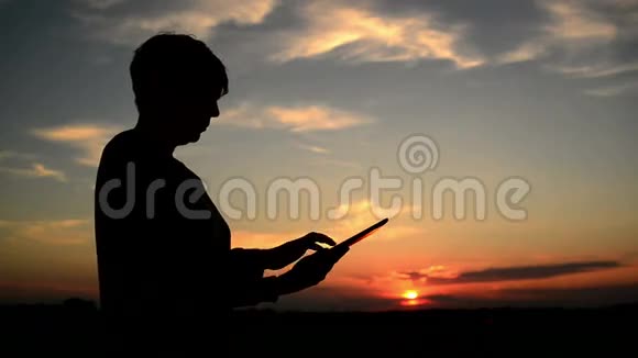 女性使用数字平板电脑上网女性剪影与现代小玩意站在日落视频的预览图