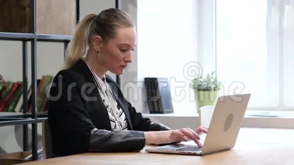 在镜头中微笑女人在笔记本电脑上打字办公室视频的预览图