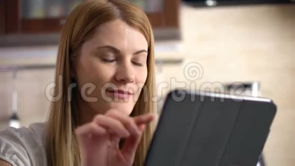 漂亮的年轻女人坐在厨房里的平板电脑浏览互联网和微笑视频的预览图