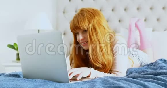 美丽的女人在床上放松时使用笔记本电脑视频的预览图