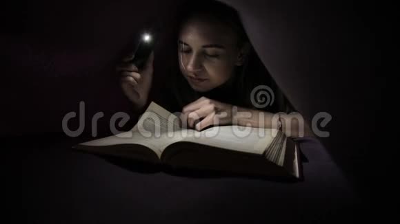 小女孩在黑暗中用手电筒在毯子下面看书视频的预览图