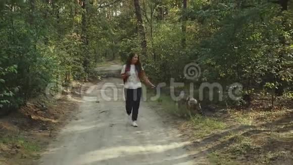 带着咖啡和狗的女孩在美丽的森林里散步女人和混种狗沿着乡村走视频的预览图