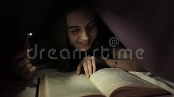 小女孩在黑暗中用手电筒在毯子下面看书视频的预览图