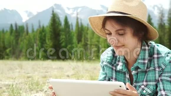 年轻女子在户外用平板电脑躺在草地上面带微笑视频的预览图