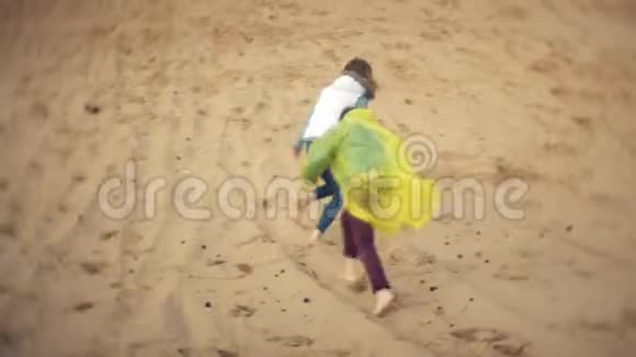 这位母亲穿着雨衣和儿子玩耍在海滩上跑下海视频的预览图