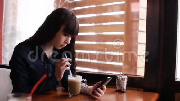 小女孩在咖啡馆里用智能手机手持的视频的预览图