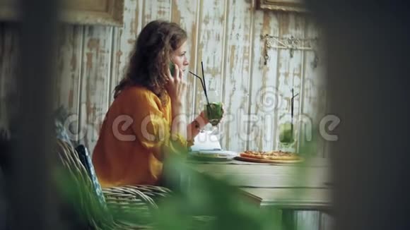 一个年轻的女人在咖啡馆的酒吧喝鸡尾酒用电话视频的预览图