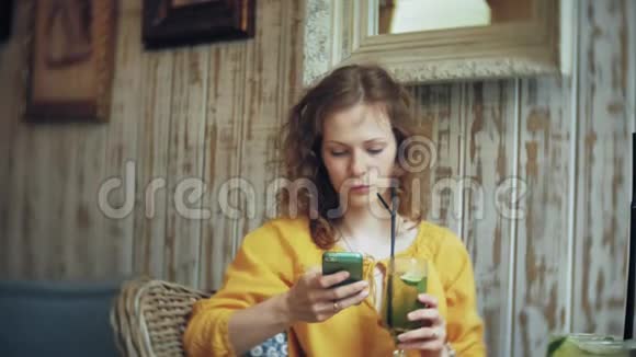 一个年轻的女人在咖啡馆的酒吧喝鸡尾酒用电话视频的预览图