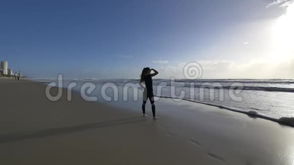 清晨美丽的年轻女性慢跑者在海滩上看太阳和海浪视频的预览图