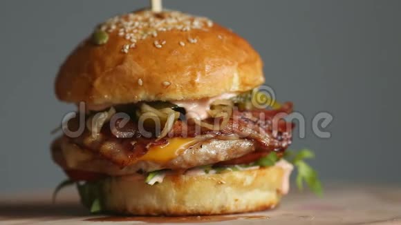 带有牛肉片西红柿蘑菇和黄瓜的大汉堡和融化的奶酪在木板上轻轻旋转视频的预览图