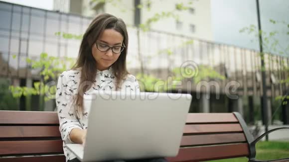 优雅的年轻女子坐在户外手提电脑远程工作视频的预览图
