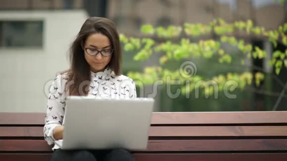 优雅的年轻女子坐在户外手提电脑远程工作视频的预览图