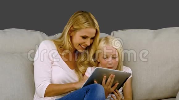 母亲和女儿在沙发上慢动作着用数字平板电脑视频的预览图