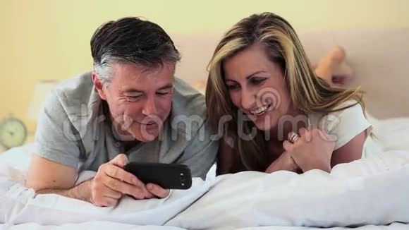 一对成熟的夫妇躺在床上看着智能手机视频的预览图