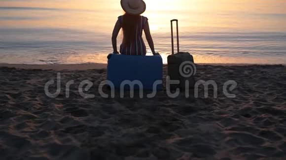 年轻女子坐在沙滩上的手提箱上视频的预览图