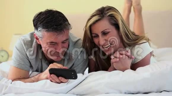 成熟的情侣躺在床上看着智能手机视频的预览图