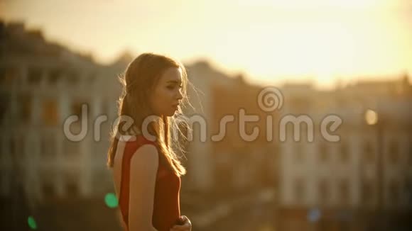 日落时分一个穿着红衣服的年轻女子站在屋顶上视频的预览图