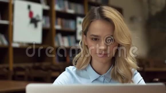 金发女人在图书馆用笔记本电脑工作视频的预览图
