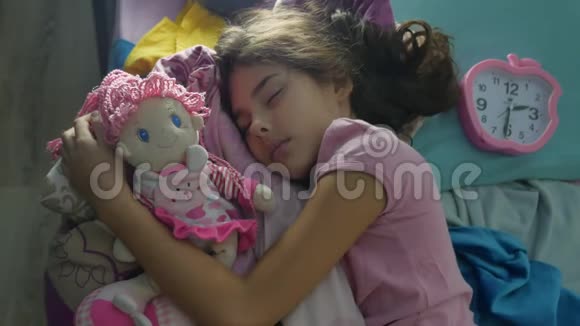 可爱的小女孩晚上睡在沙发床上在室内拥抱她的娃娃女孩深肤色的少年可爱的睡着了视频的预览图