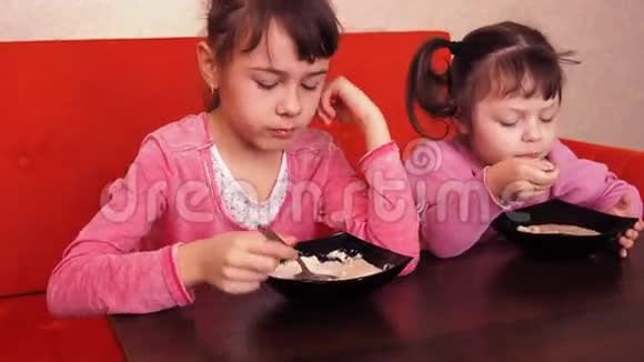 孩子们吃粥两个小女孩吃粥两个姐妹坐在橙色的沙发上吃晚饭视频的预览图