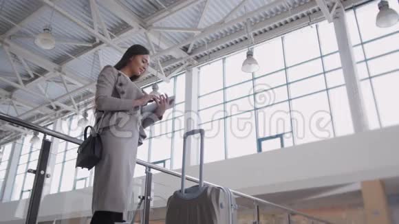 美丽的年轻女子在机场使用平板电脑优雅的女商人带着手提箱等待着飞机视频的预览图