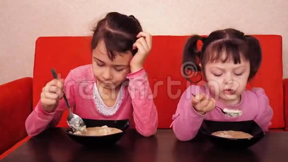 孩子们吃粥两个小女孩吃粥两个姐妹坐在橙色的沙发上吃晚饭视频的预览图